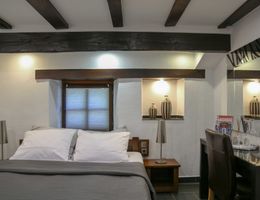 Ein gemütliches Hotelzimmer mit einem Doppelbett, Holzbalken an der Decke, einem kleinen Tisch mit Stuhl und dekorativen Vasen in einer Nische.