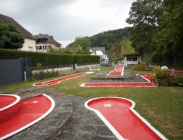 Minigolfanlage in Vianden mit roten Bahnen, Steinwegen, Bäumen und Häusern im Hintergrund.