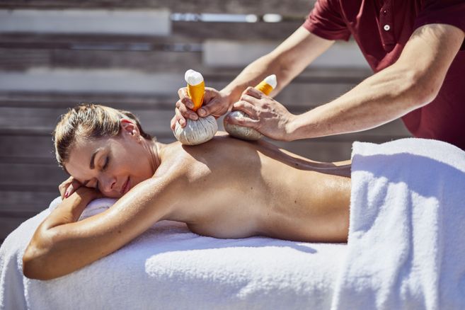Massage aux tampons pratiqué sur une dame allongée sur le ventre. 
