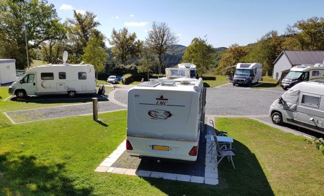 Wohnmobile auf einem Campingplatz in Liefrange, Luxemburg, umgeben von Bäumen und Hügeln.